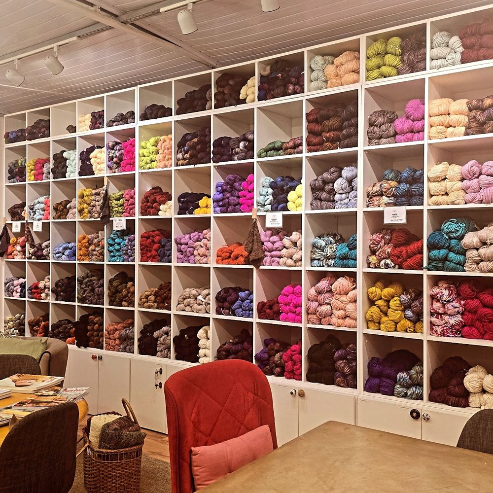 Interior de uma loja de artes manuais mostrando uma estante grande com vários novelos coloridos. 
