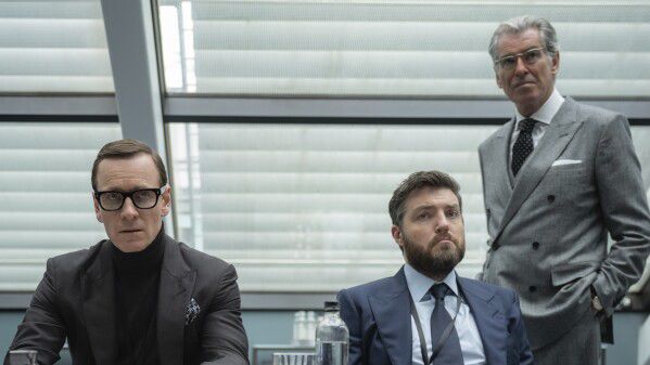 Men in suits, still from Black Bag.

From left: Michael Fassbender (seated, chunky black glasses and black turtleneck); Tom Burke (bearded, single breasted charcoal suit and necktie); and Pierce Brosnan (grey double breasted, standing).