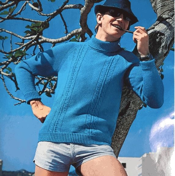 A man in a dark blue fedora, sky blue sweater and light wash denim-colored short shorts with a pipe in his mouth, leaning against a tree
