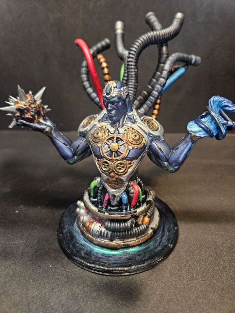 A miniature mechanical man rises out of an oily base with a large amount of tubes and wires connected to him.  