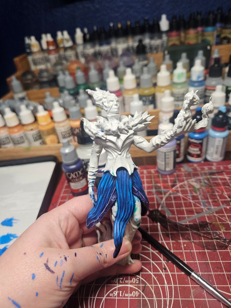 A hand holds a miniature of a man with chest armor and flowing blue skirt.