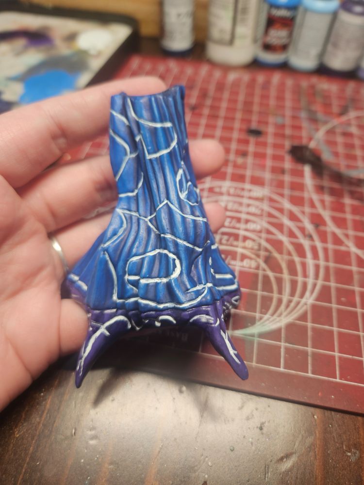 A hand holds a miniature blue cloak with swirling white lines