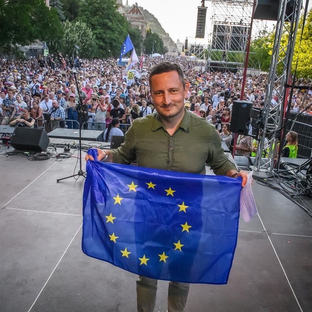 Nicolae Ștefănuță holding an European flag on stage of Budapest Pride with the crowd behind him