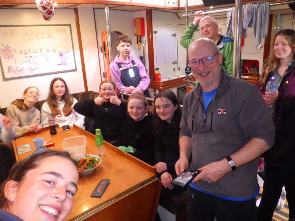 A group of young people sit around the saloon table with their sea staff.