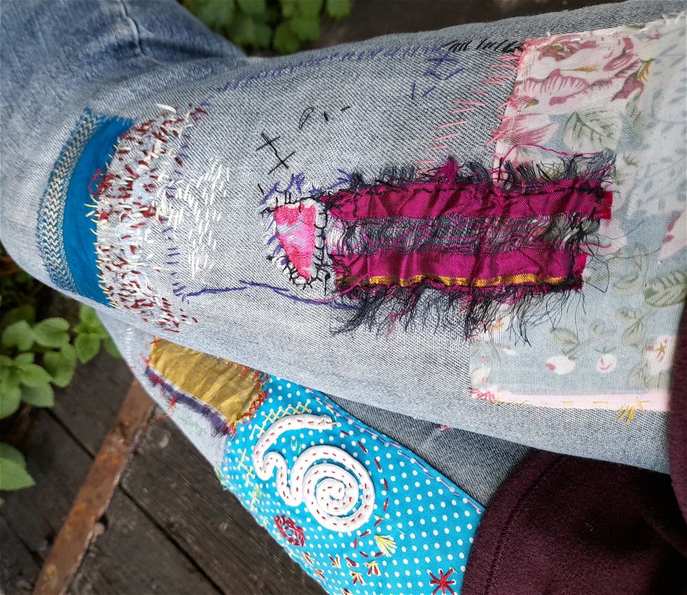 A very coulourful jeans with visible mending. Silk patches and wild embroidery in many colours to cover the holes.
