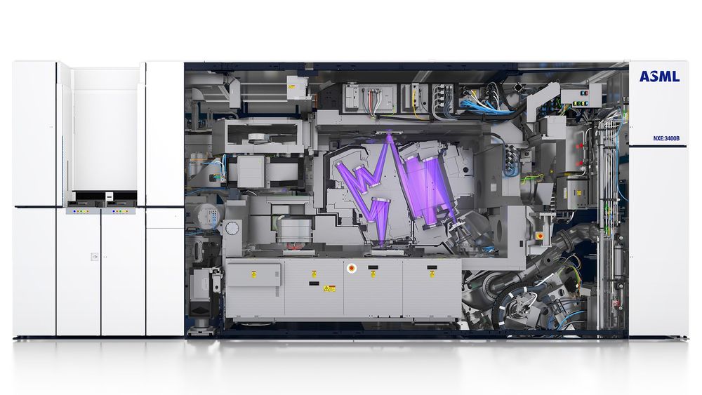 The picture shows an ASML lighography tool of the size 10x4x4 meters. It is a schematic with the main focus on a complicated projection optic. A from an EUV light source a beam hits a photo mask via multiple lenses and mirrors. From the mask the pattern is transferred to a wafer which is placed on a stage. This projection optic is embedded in a vacuum chamber and surrounded by lots of wiring.