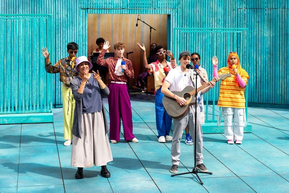 A group of young people performing on stage along with Clare Edwards, Integrated BSL Interpreter in The Two Gentlemen of Verona. Photograph: Sara Beaumont