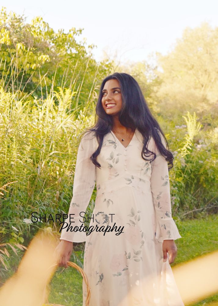A senior graduation photoshoot of a high school senior walking with a wicker basket in hand, as they stroll along tall grasses. 
