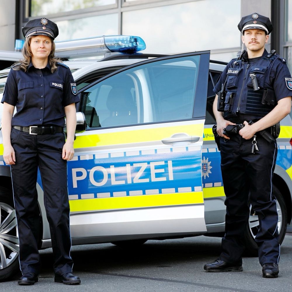 Eine Polizistin und ein Polizist vor einem Polizeiauto