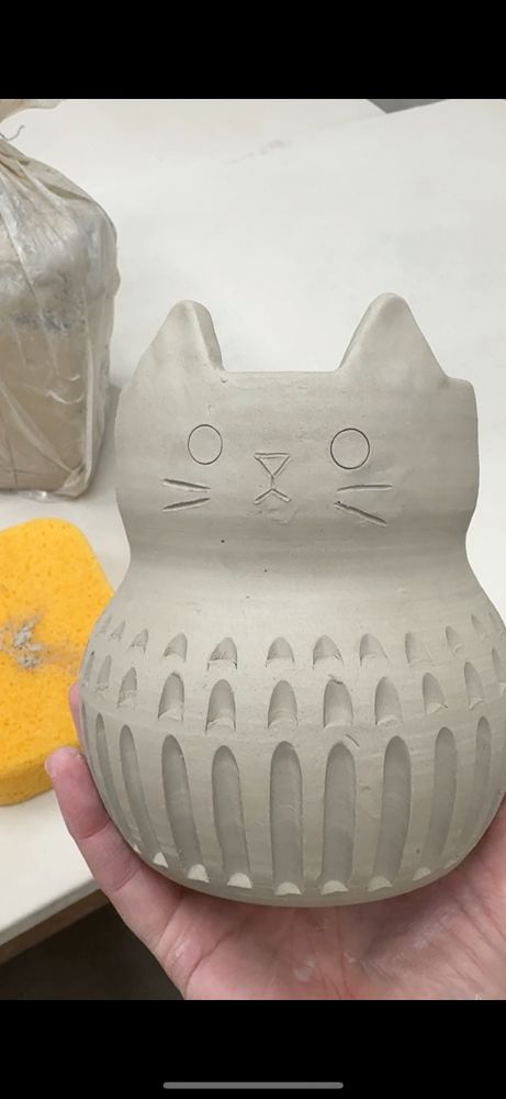 A handmade wheel thrown vase with carving on the bottom and cat ears and a cat face. 