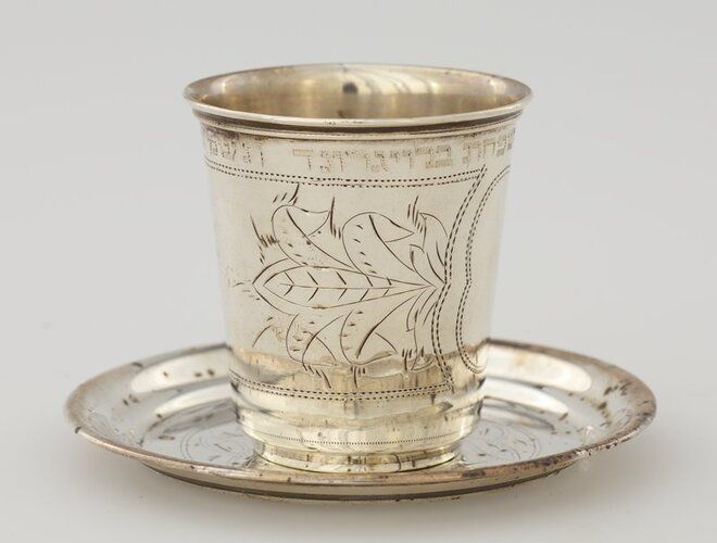 small tumbler-style cup; band with organic designs and central cartouche; text above; saucer has organic designs flanking a shield, inside a circle