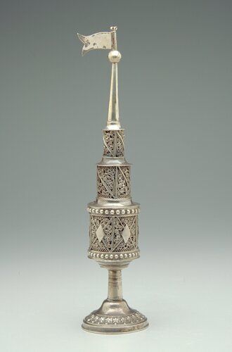 three-tiered circular tower with movable flag at top on a circular footed stem base; the bottom tier has a door with latch; the walls of all tiers done in openwork filigree
