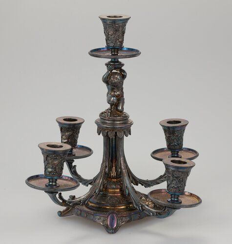 highly decorated silver with gilt trim; four candle holders on arms radiating from central pillar; squatting satyr holding central candle holder above his head