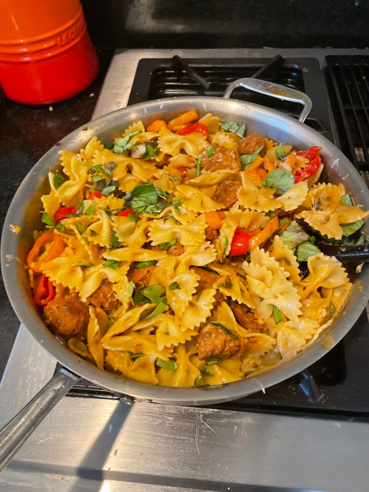 Farfalle pasta with sausage bits, sautéed bell peppers, and basil sprinkled on top. 