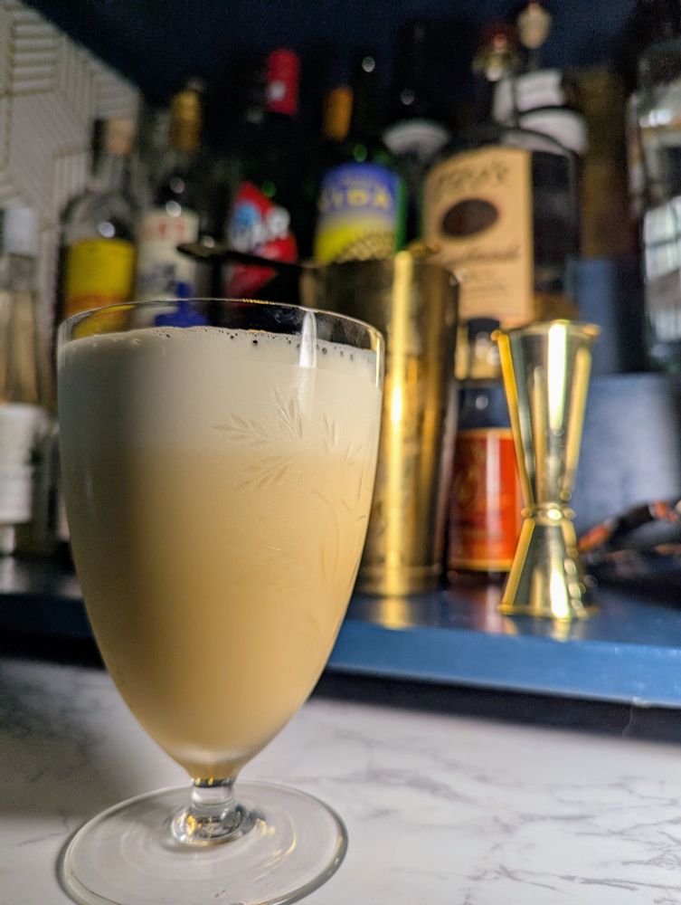 A light brown creamy milkshake-like cocktail in front of a small dry bar.
