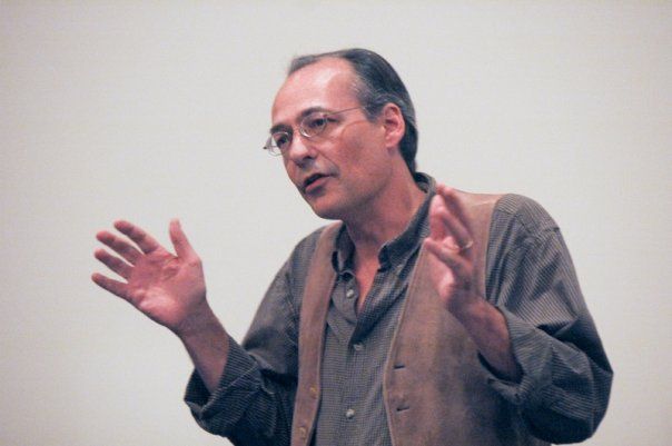 handsome bespectacled balding man gesticulating in his only vest
