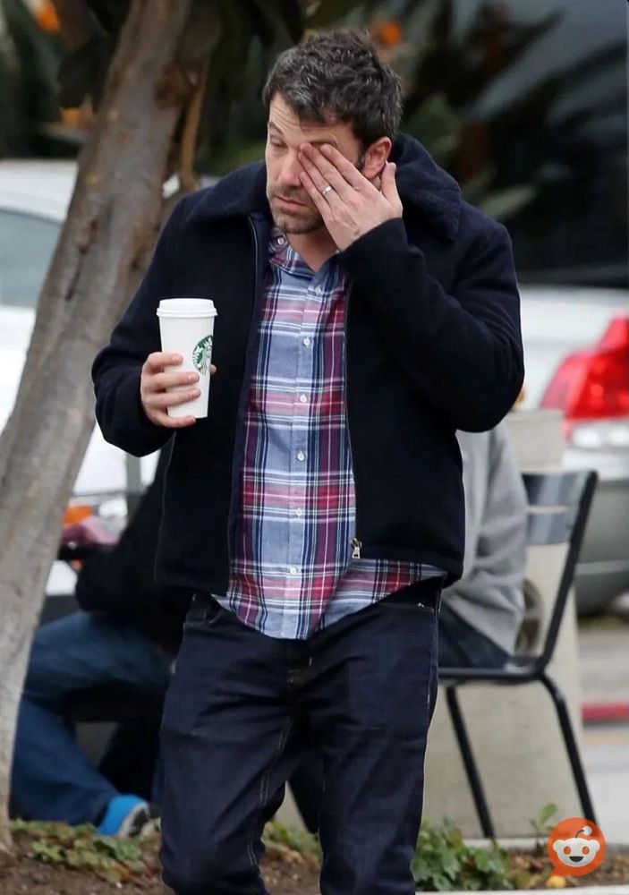 Paparazzi photograph of an exhausted Ben Affleck wiping his face while holding a large coffee cup.