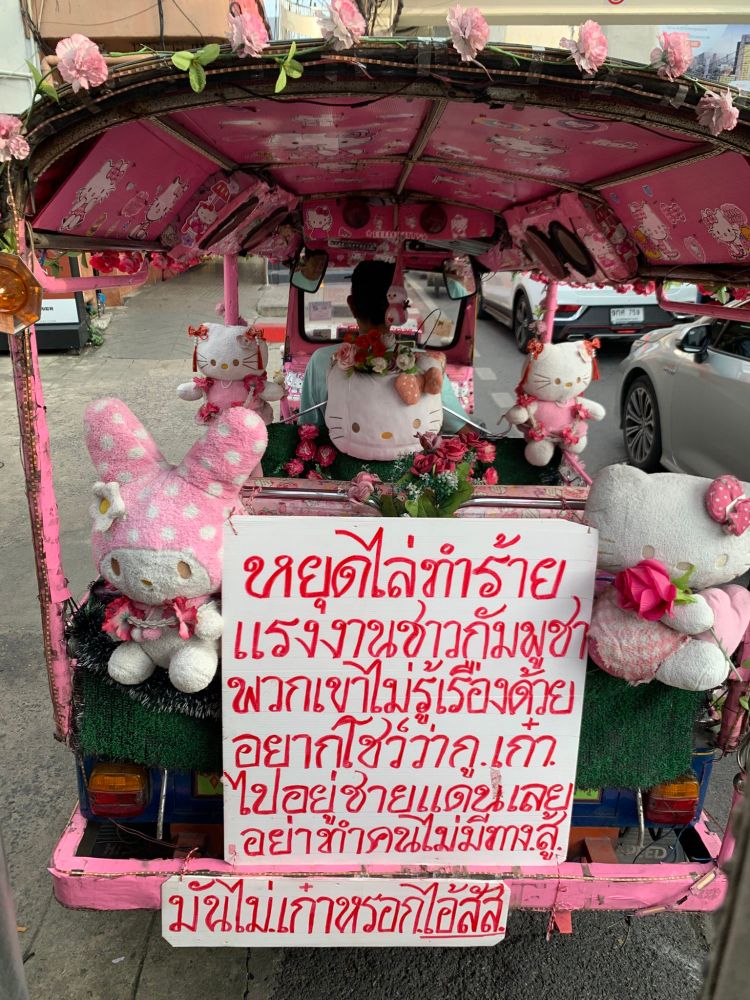 A hello kitty themed tuk-tuk with a plushies, a hello kitty branded roof in pink has a sign in back that says in thai.

“Stop harming Cambodian workers. They don't know anything about this. If you want to show off how cool you are, go live at the border instead. Don't pick on people who can't fight back. That's not cool at all, you bastards.'"