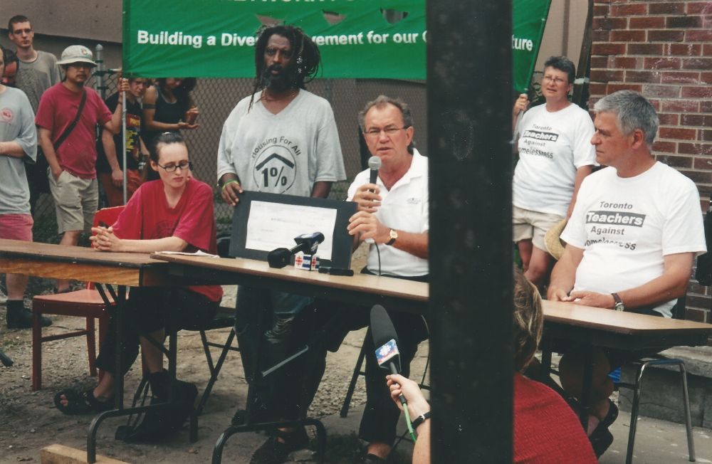 Several people sitting at a table outdoors, holding microphones. 