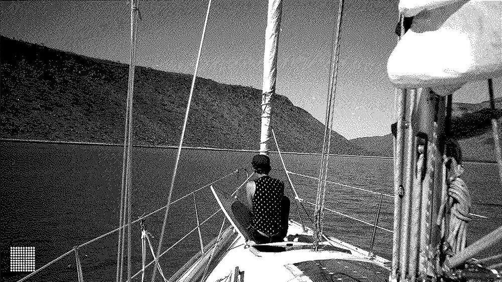Grainy black and white image of a person sitting at the prow of a ship.