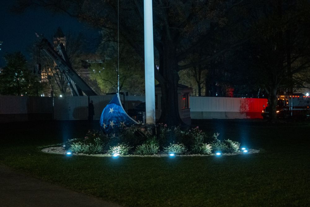 US flag at the White House attached to a flag pole but laying on the ground. 