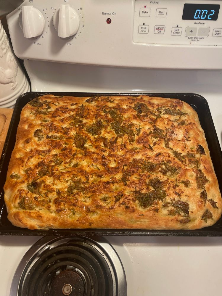 A fresh pan of Foaccia bread coated in rosemary and garlic cools on a pan 