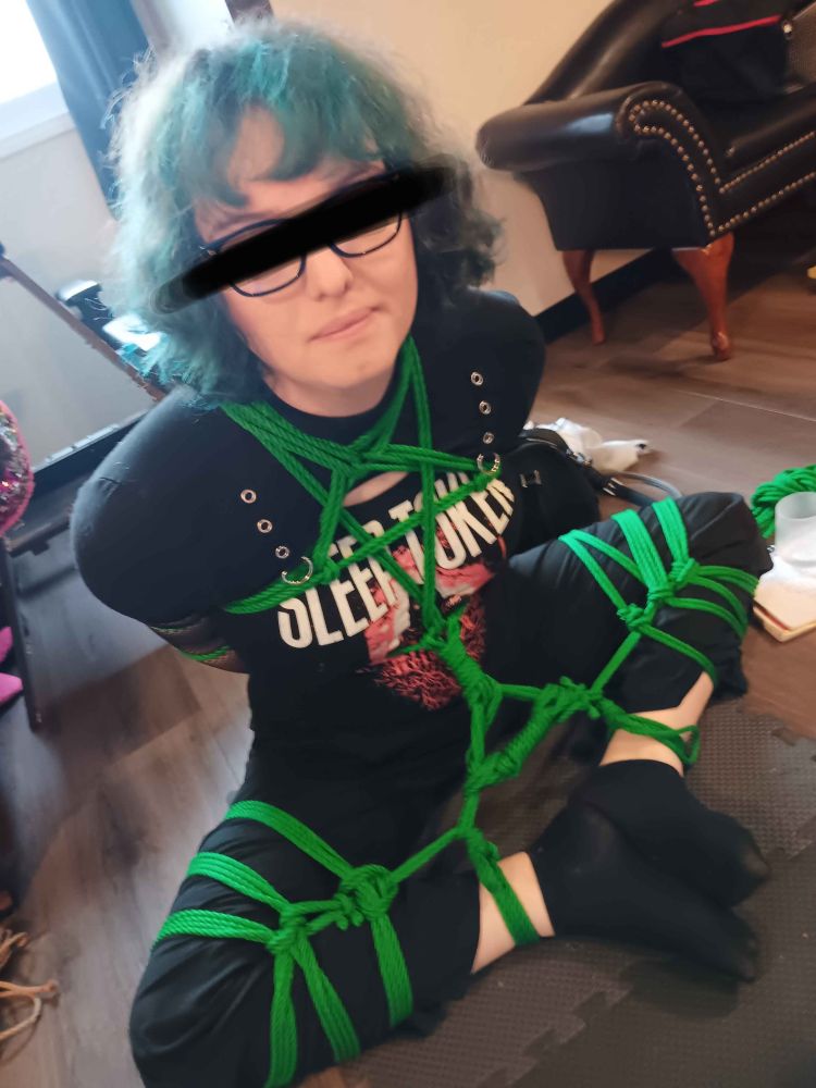 A pretty girl frogtied with her arms behind her and her chest rigged to her ankles