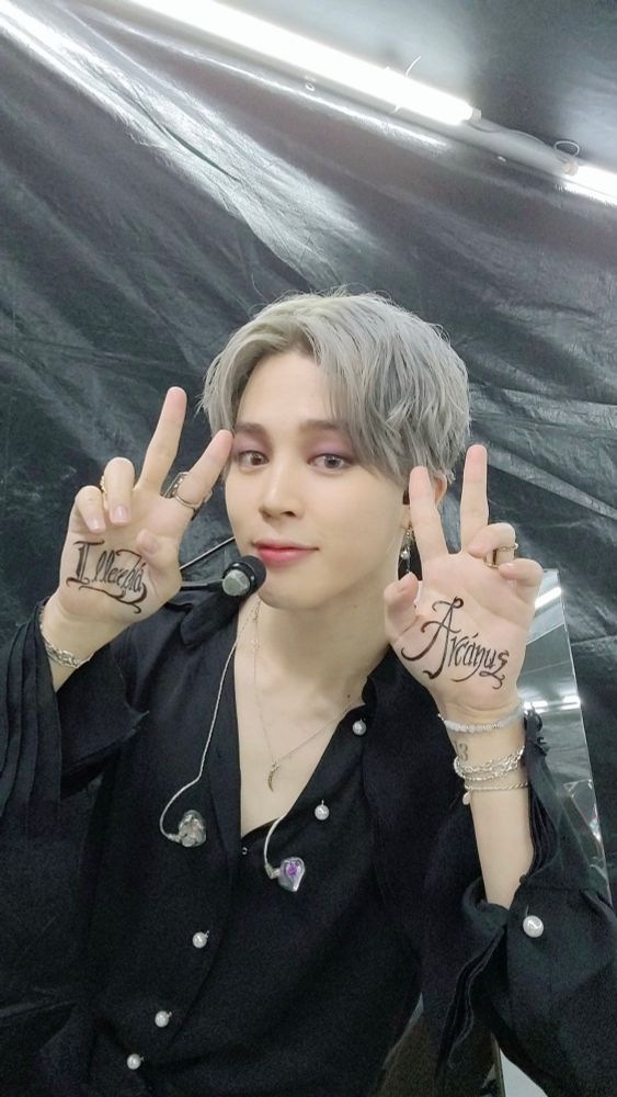 BTS Jimin, blonde hair, wearing a black shirt, during the recording of the song Filter for day 2 of the online concert Map Of The Soul ON:E. He shows the words “Illecebra” and “Arcanus” that are written on his palms into the camera. 