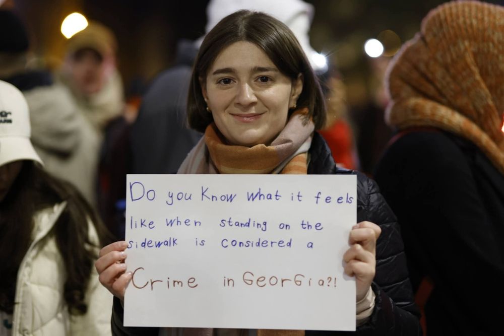 Young girl holds during protests a sign with question "“Do you know what it feels like when standing on the sidewalk is a crime?”