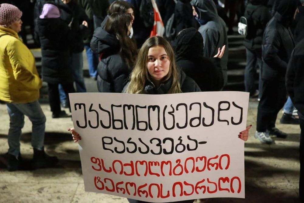 Photo of activist Natia Gabrava who wrote a Facebook post in solidarity with Ia Melitauri. She holds a large handmade sign with text like this:
unlawful  arrest is an act of psychological terror