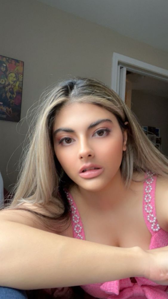 I’m a young woman with olive skin and dark blonde hair. I’m looking into the camera with a neutral facial expression while wearing a pink dress.
