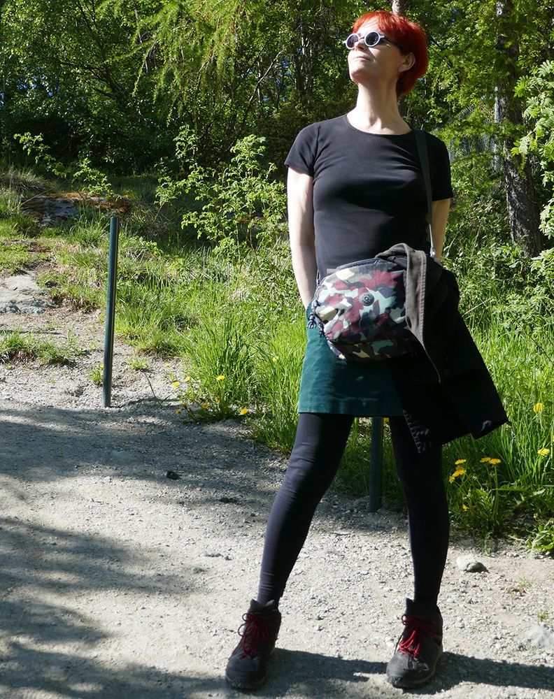 Photo of Alexandra standing on a path in the countryside wearing sunglasses black t-shirt and green skirt 