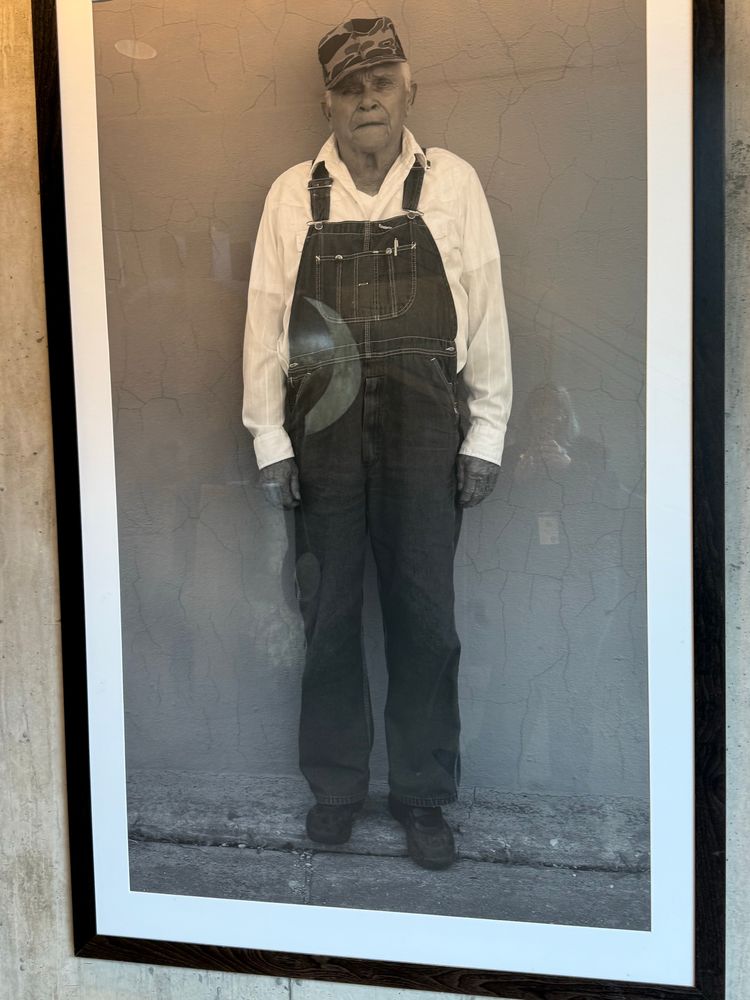 Ed Cox once again in 2007 in another black and white photo. he has a white shirt on and overalls and a camo hat. 