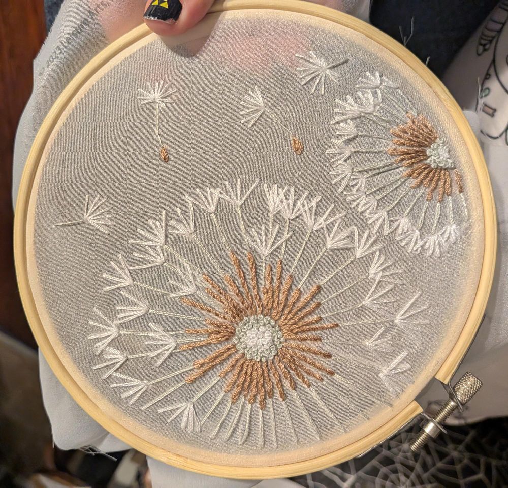 An embroidery project of two dandelions gone to seed, stitched on sheer fabric 