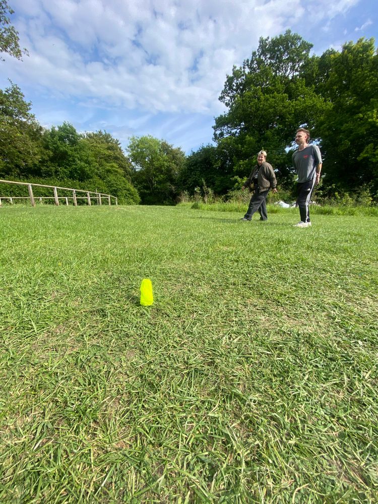 A small nuclear standing stone in an expanse of grass. To the right two people are walking across the grass and smiling 