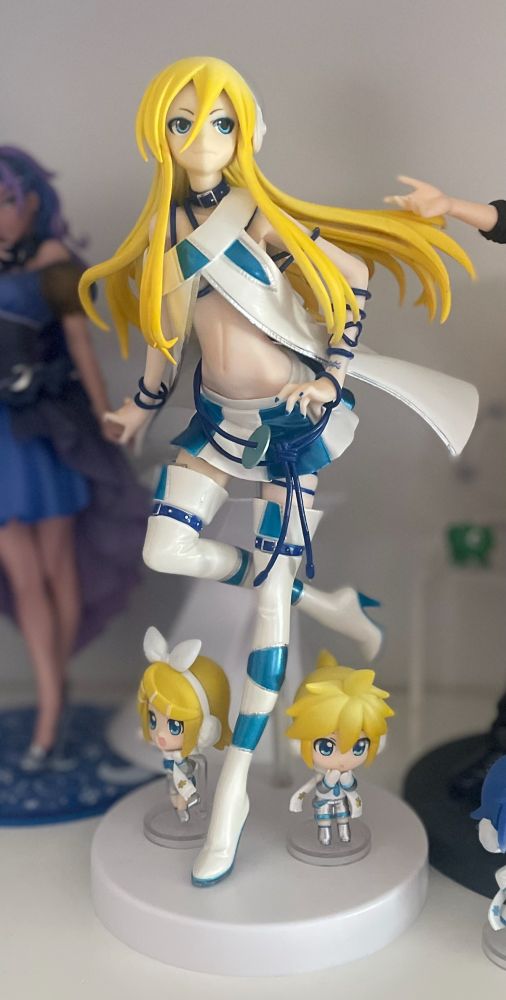 Photo of a Vocaloid Lily statue of her ice outfit. On the white base of the figure, are two smaller figures of Rin and Len in their snow modules as nendoroid petites.