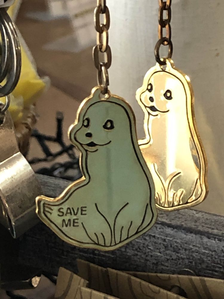 a seal keychain (metal, 2D style) with SAVE ME (in all caps) pressed into the metal on the tail part