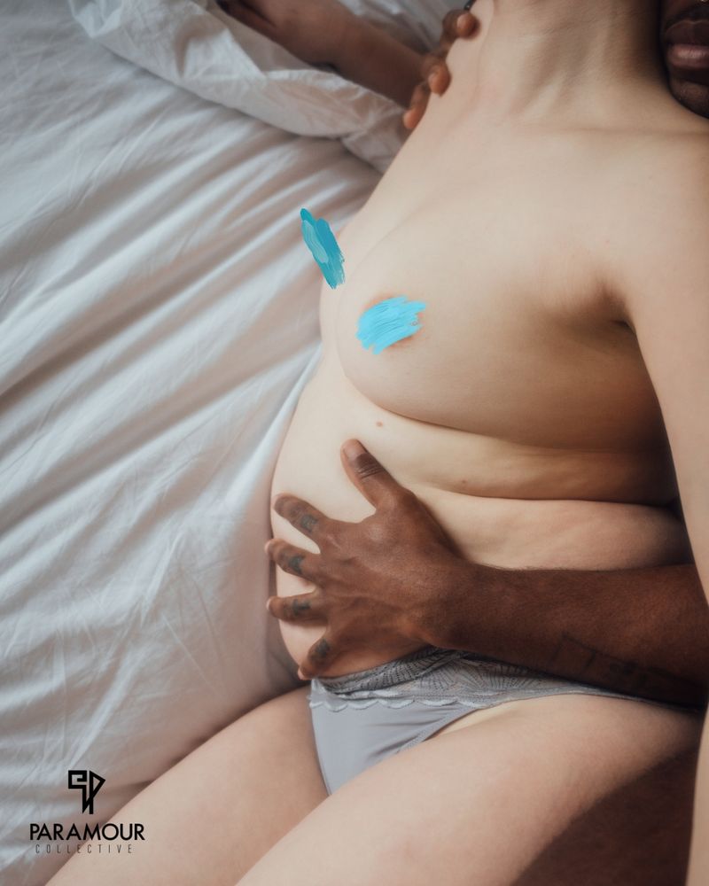 a soft white femme body is being held by a strong black masc body, his arms wrapped around her stomach. they lie on crumpled white sheets

