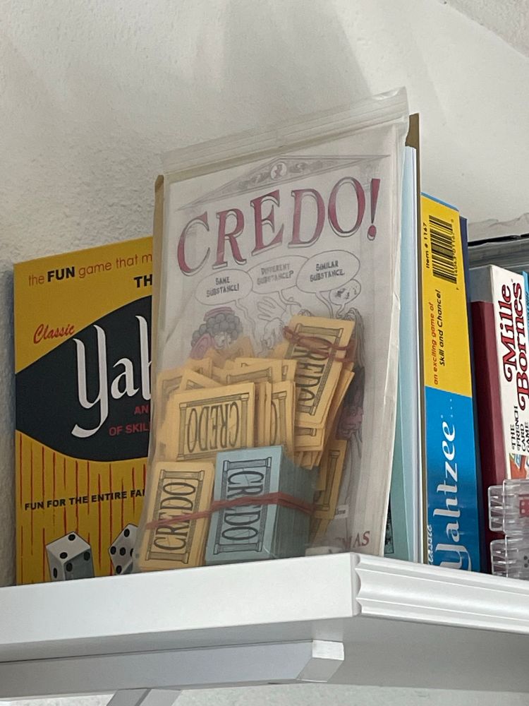 Ziploc copy of the 1993 Chaosium card game “Credo!” sitting on a shelf alongside copies of Yahtzee and Mille Bornes and a couple other unidentifiable games