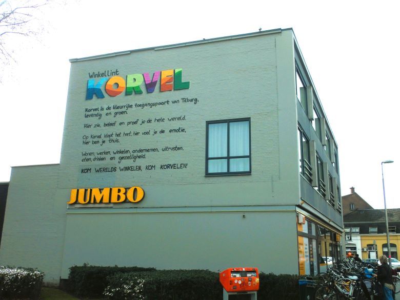 Gevelwand in Tilburg met een tekst over winkelgebied Korvel  Volgens de tekst klopt er het hart, voel je emotie en ben je er thuis. 
Wonen, werken, winkelen, ondernemen, uitrusten, eten, drinken en gezelligheid. 
Kom werelds winkelen. 

Daaronder het logo van supermarktketen Jumbo