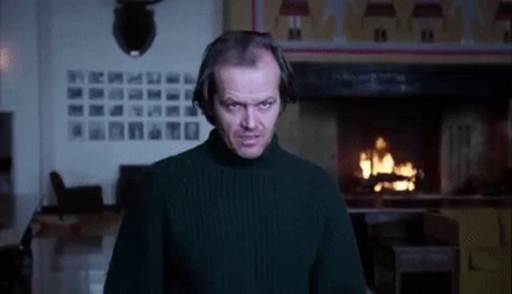 a man in a turtleneck sweater is standing in front of a fireplace .