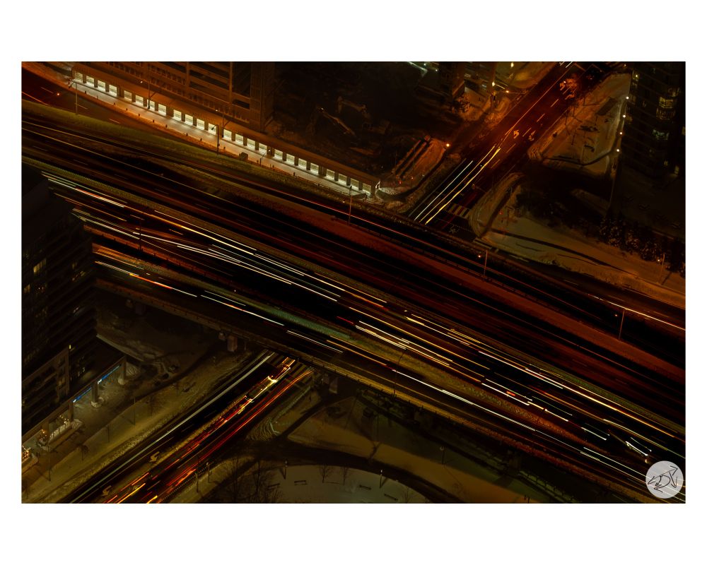 A long exposure photo of traffic with the traffic traveling north & south going under a bridge of the traffic going east & west