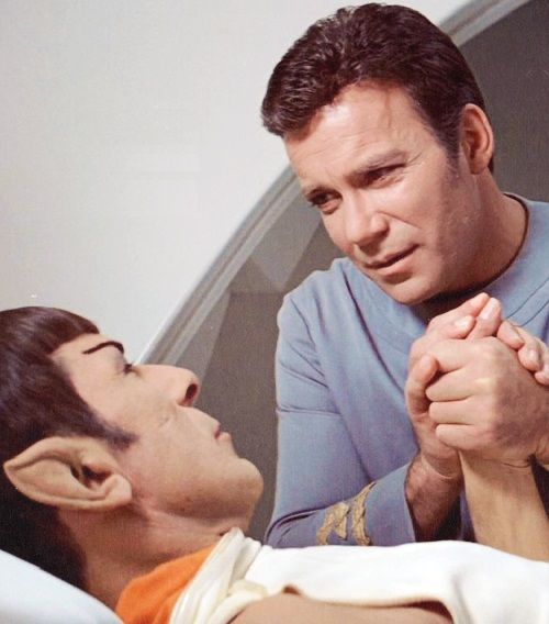 A still image from the film "Star Trek: The Motion Picture" showing Spock lying in a medical suite bed with Kirk holding his hand.