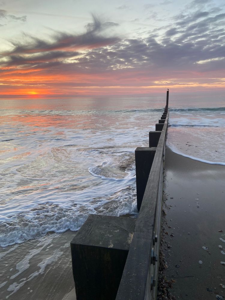 Sunrise over the sea, looking along a groyne.