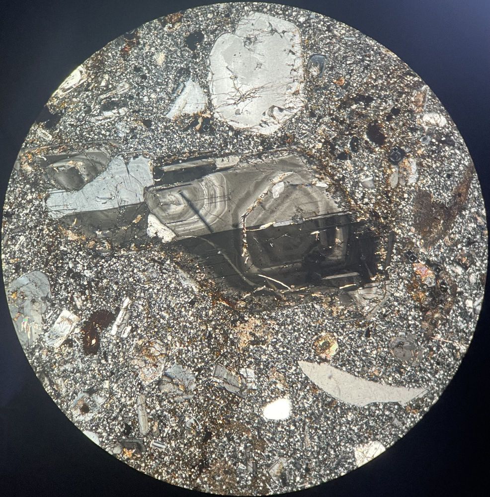 Felsic minerals in cross polarised light from Bau Granite Suite in Borneo. Large phenocryst in centre shows two regions of concentric zoning. Several other plagioclase phenocrysts show concentric zoning and twinning. Crescent shaped crystal (bottom right) is very rounded quartz xenocryst. Very fine grained groundmass of feldspars and quartz.