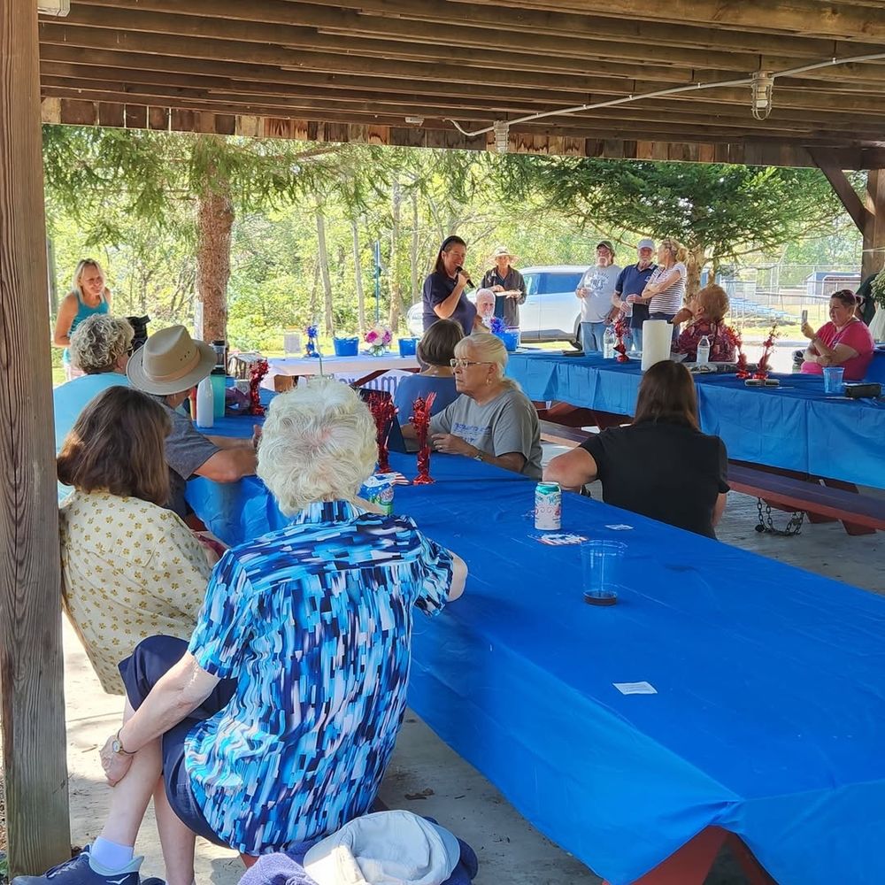 Beth Farnham (woman with microphone) and people at picnic tables in a pavilion.