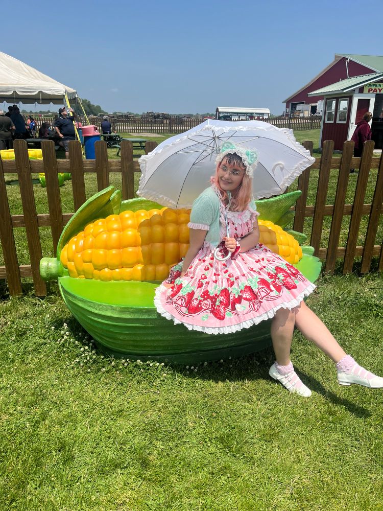 The same person from the first photo posing on a bench shaped like a giant ear of corn