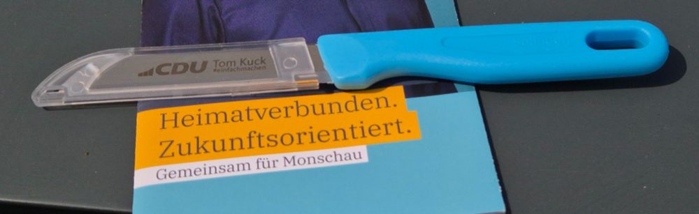 Foto einer Postwurfsendung der CDU. Zu sehen ist ein Küchenmesser mit CDU-Logo auf der Klinge, sowie blauem Griff, dies liegt auf einem Flyer "Heimatverbunden. Zukunftsorientert. Gemeinsam für Monschau."