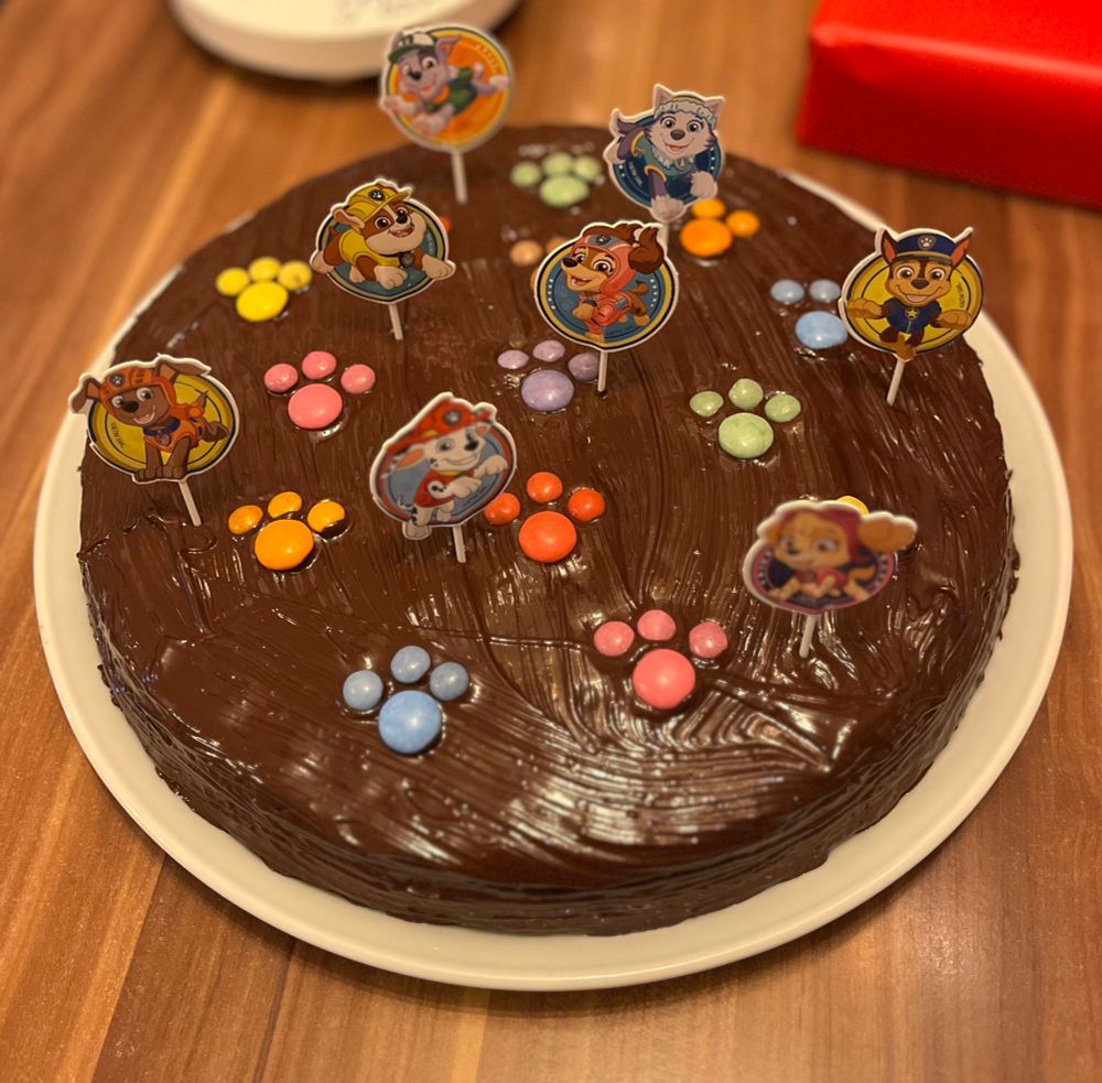 Schokokuchen mit Pfoten aus schokolinsem darauf. Kleine Paw Patrol Kuchenstecker befinden sich im Kuchen.