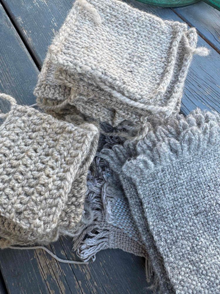 Three piles of grey swatches on a stained wooden surface. Clockwise from bottom-left: crochet, knitting, and weaving.